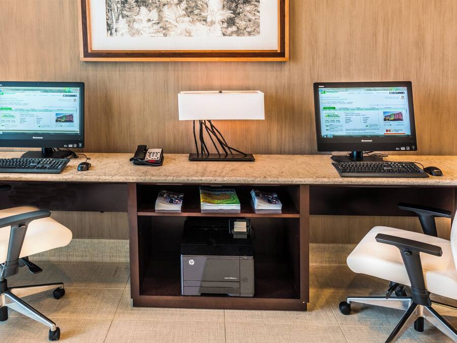 Ein Hotelbüro mit zwei Monitoren, einer Schreibtischlampe, einem Telefon und einem Drucker.