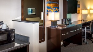 Une chambre d’hôtel équipée d’une kitchenette, d’un grand miroir, d’un téléviseur à écran plat, d’un bureau avec une lampe et d’un lit avec une tête de lit.