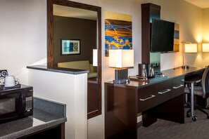 A hotel room with a kitchenette, a large mirror, a flat-screen TV, a desk with a lamp, and a bed with a headboard. - Holiday Inn Paducah Riverfront by IHG (Paducah)