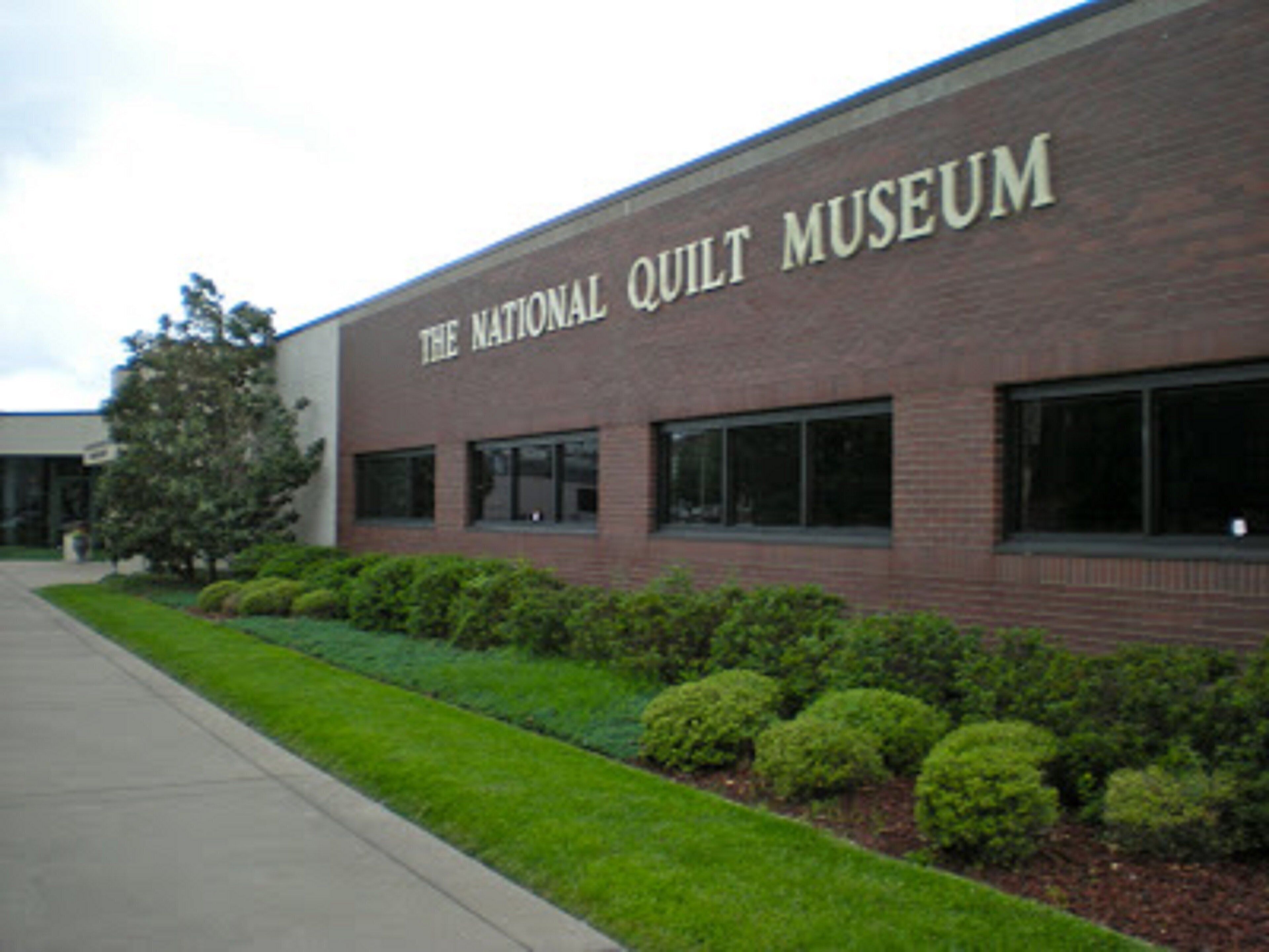 The exterior of The National Quilt Museum with a brick facade, large windows, and a well-maintained lawn.