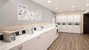 Une buanderie équipée de plusieurs machines à laver et de plusieurs séchoirs, d’un panneau de commande et d’affiches informatives sur les murs.