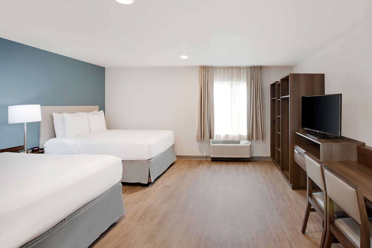 A hotel room with two beds, a desk with a TV, a lamp, and an air conditioning unit.
