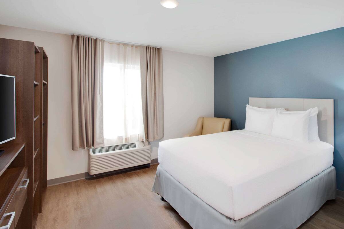 A hotel room with a bed, a TV, a wardrobe, and a window with curtains.