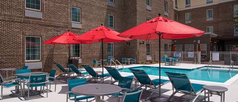 A poolside area with multiple red umbrellas, lounge chairs, and tables.