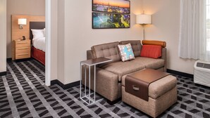 Ein Hotelzimmer mit Sofa, Hocker, Nachttisch, Lampe und einem Stadtbild an der Wand.