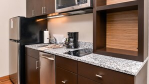 Eine kompakte Küche mit Edelstahlkühlschrank, Mikrowelle, Kaffeemaschine und Geschirrspüler.