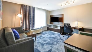Ein Hotelzimmer mit Sofa, Schreibtisch, Stuhl, Fernseher und Lampe.