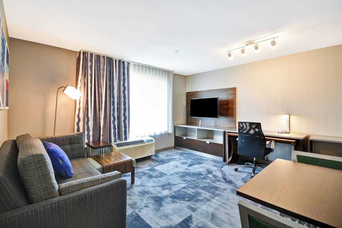 Ein Hotelzimmer mit Sofa, Schreibtisch, Stuhl, Fernseher und Lampe.