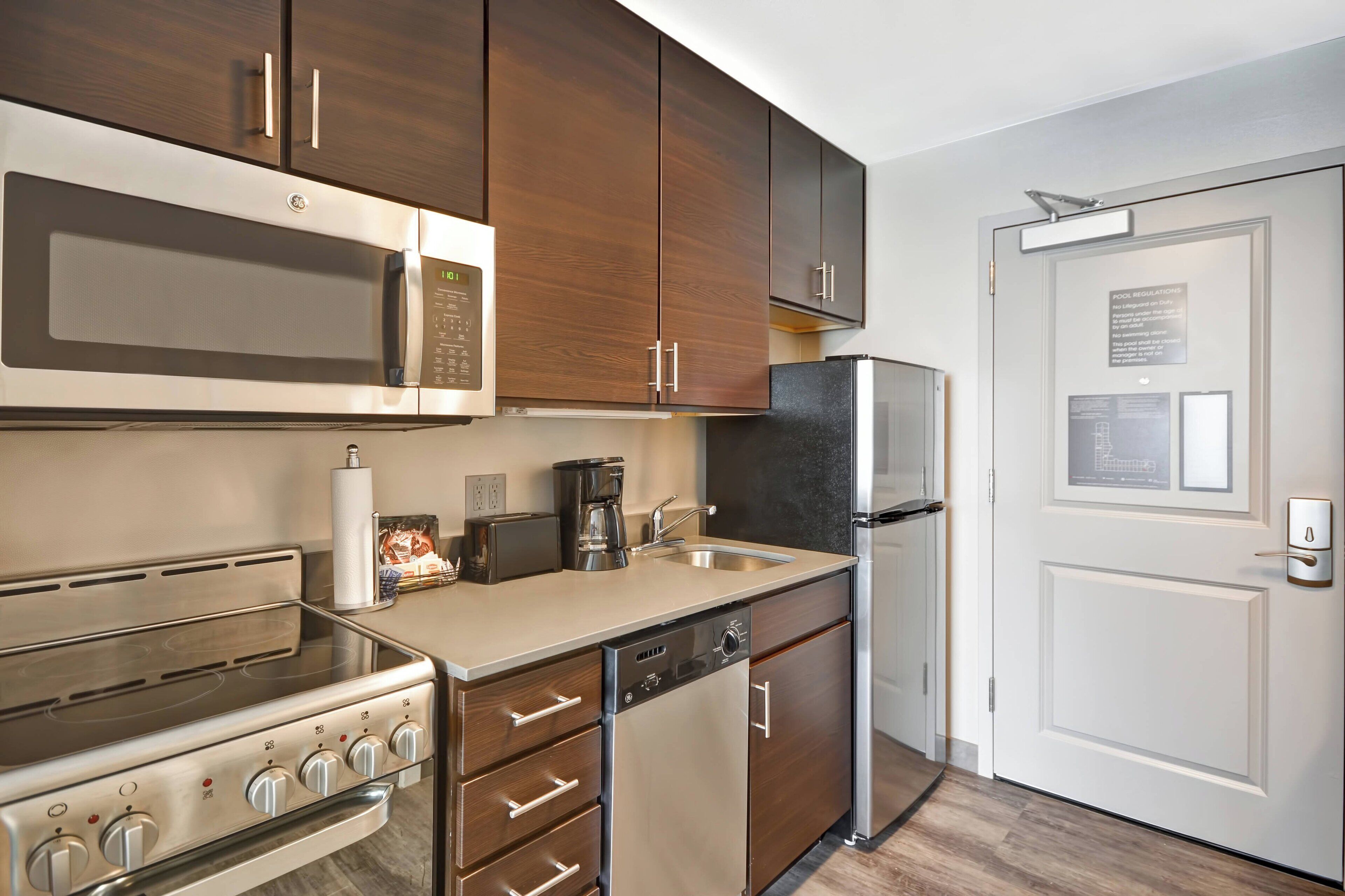 A modern kitchen with stainless steel appliances, wooden cabinets, and a built-in dishwasher.