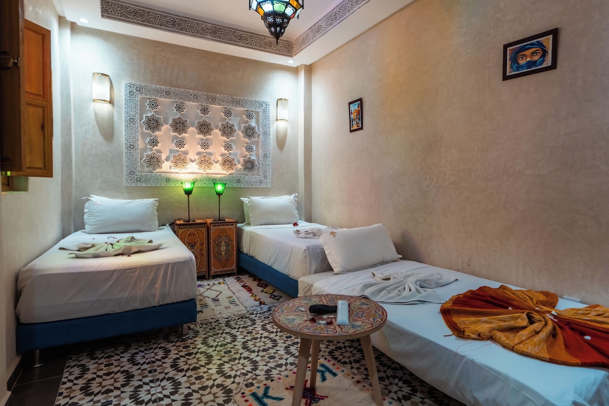 A hotel room with two beds, a small table, a decorative wall, and a patterned floor.