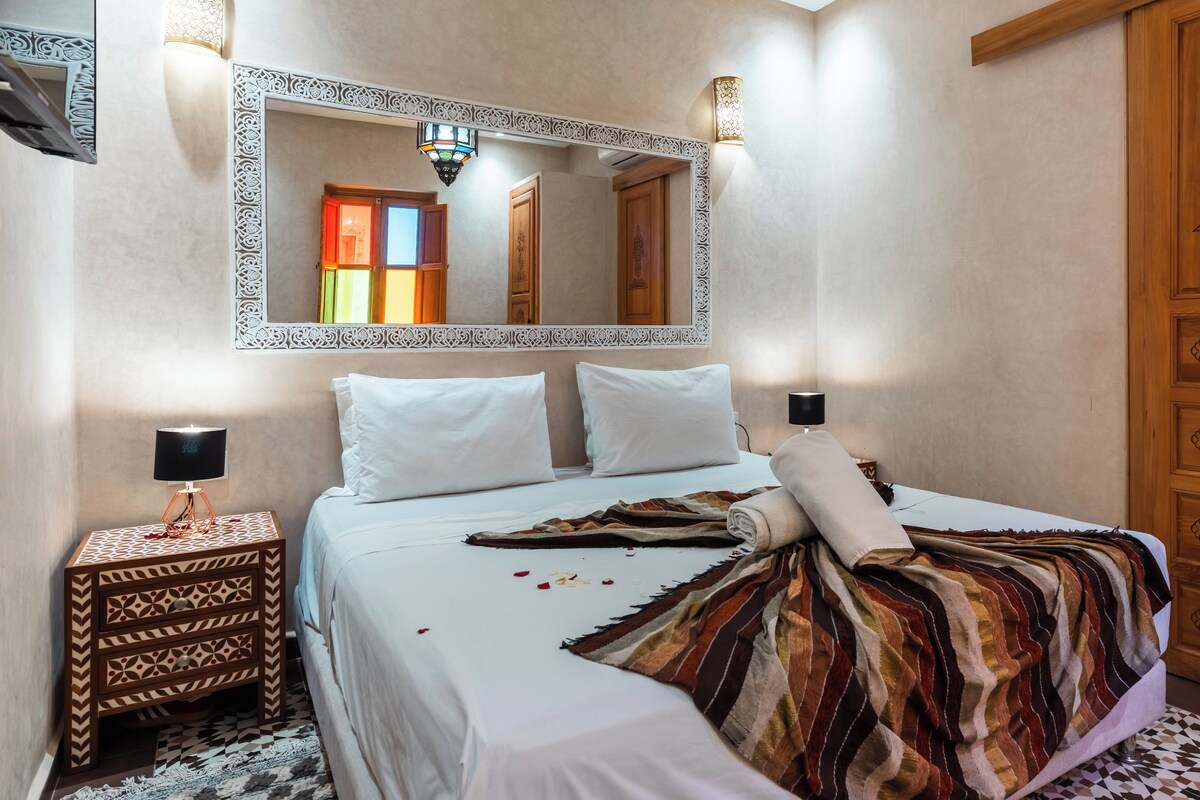 A hotel room with a bed, a nightstand, a mirror, and a wardrobe.