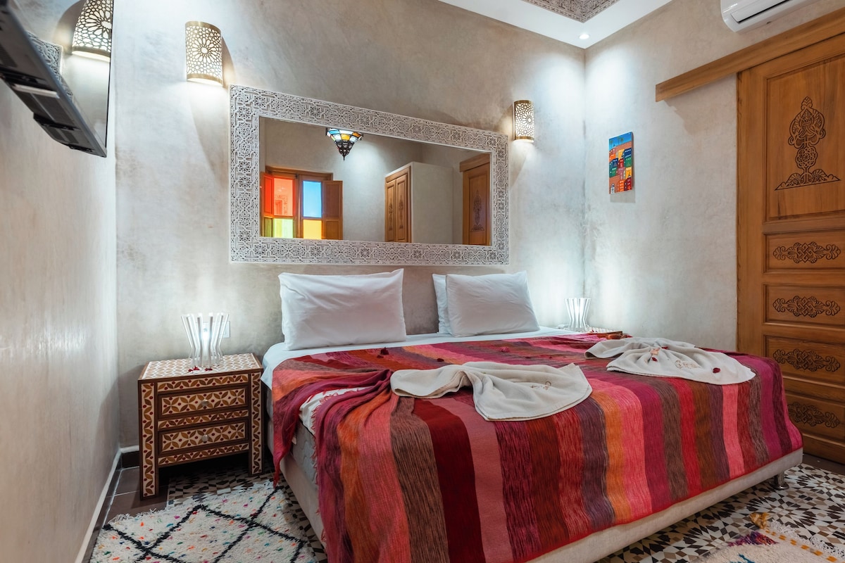 A hotel room with a large bed, a wooden wardrobe, a nightstand, and a decorative mirror.
