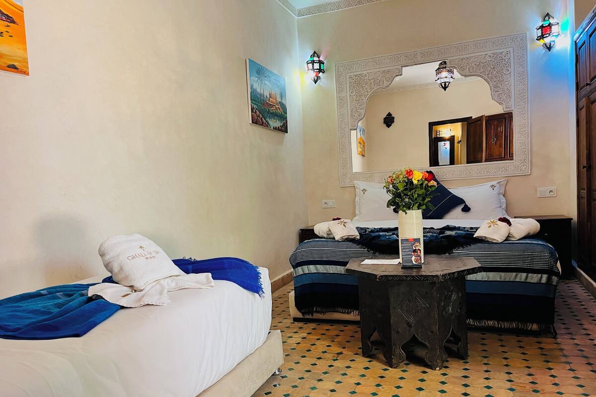 Een hotelkamer met twee bedden, een tafeltje met een bloemenvaas, en een decoratieve spiegel boven de bedden.