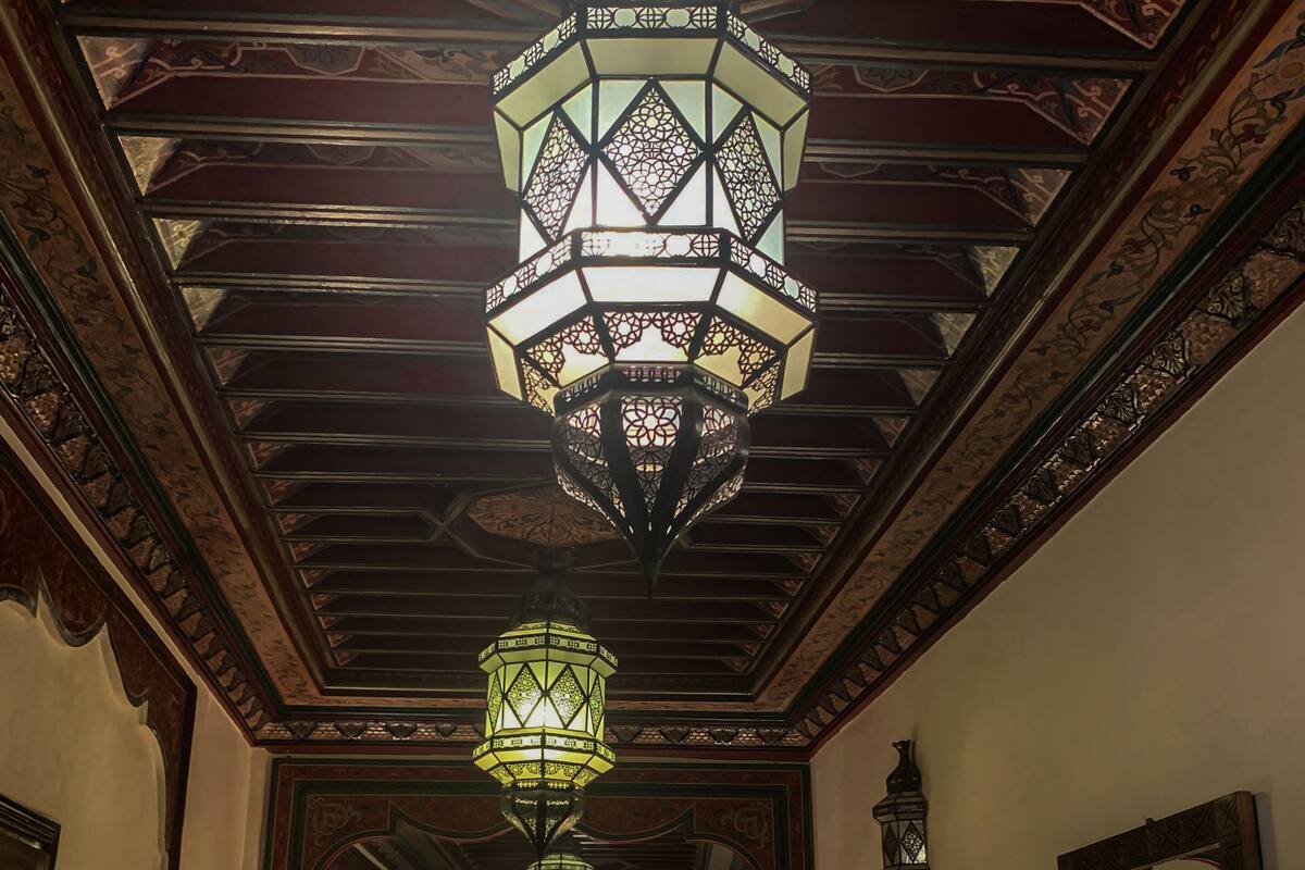 Een hotelkamer met een bed, twee bedlampjes, een grote spiegel en een decoratief plafond met ingewikkelde patronen.