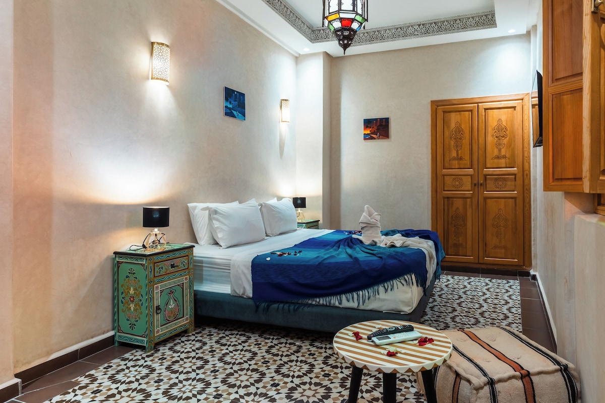 A bedroom with a bed, bedside tables, a wardrobe, and patterned floor tiles.