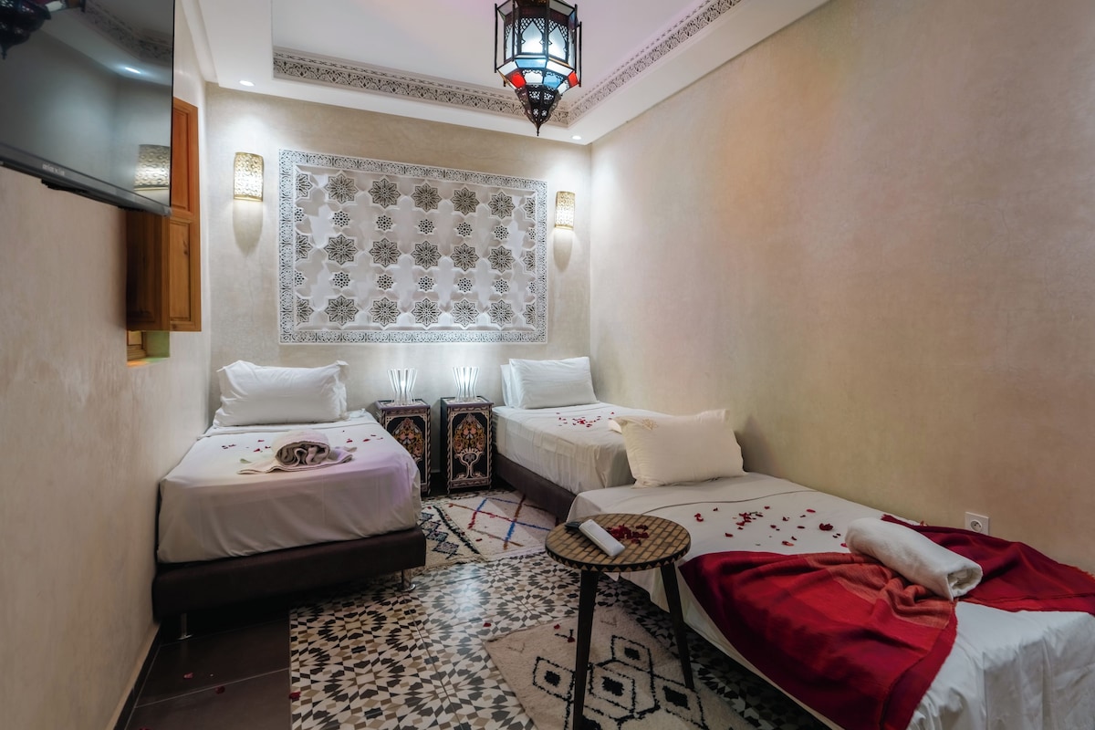 A hotel room with two beds, a patterned wall, a decorative ceiling light, and a small round table.
