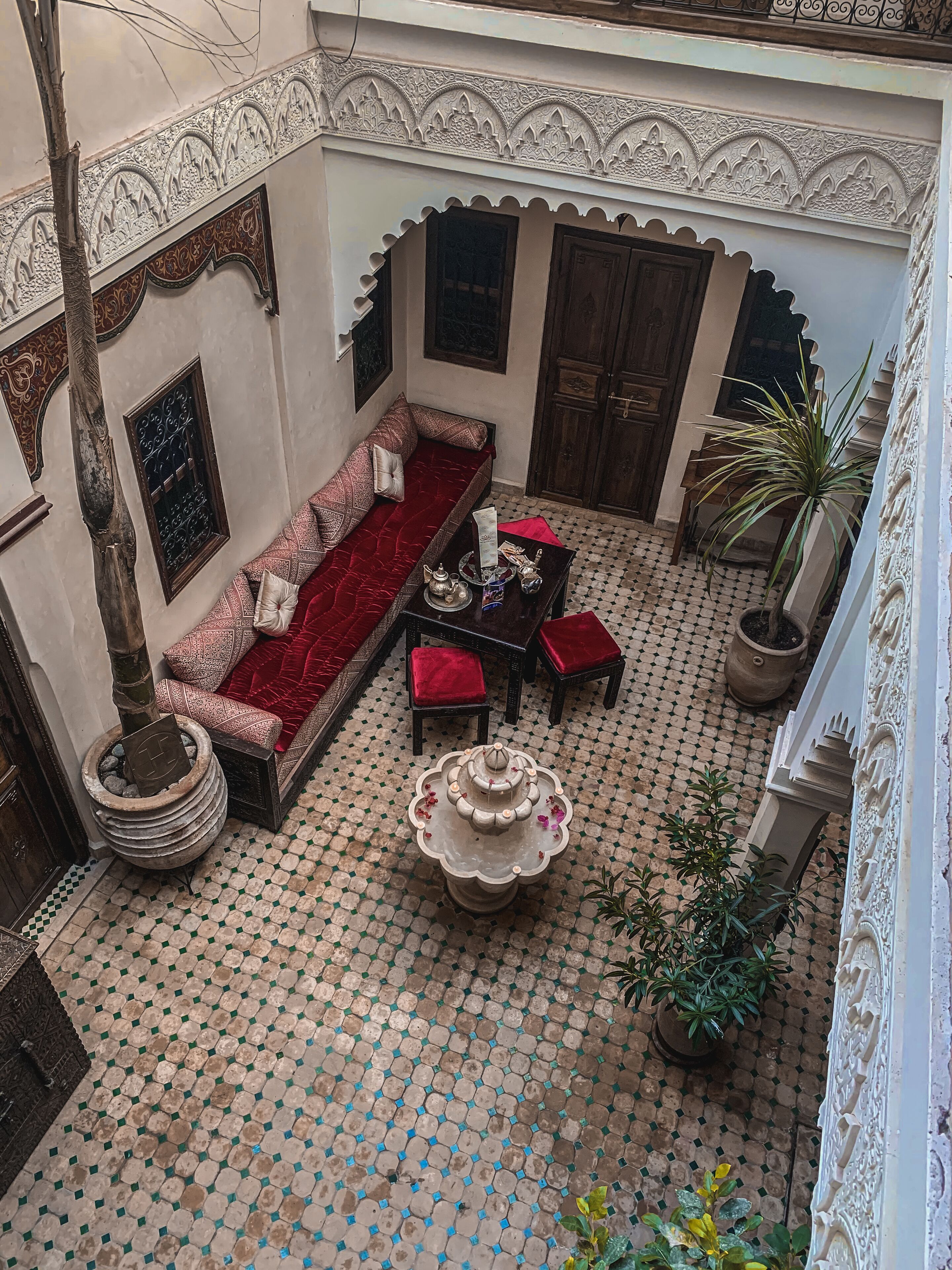 Une cour avec un canapé rouge, une table ornée d’une fontaine et des plantes en pot.