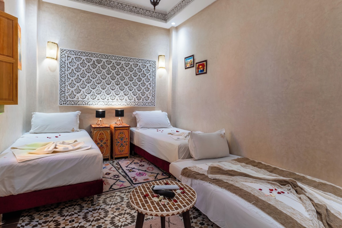 A hotel room with two beds, a small table, and a decorative wall panel.
