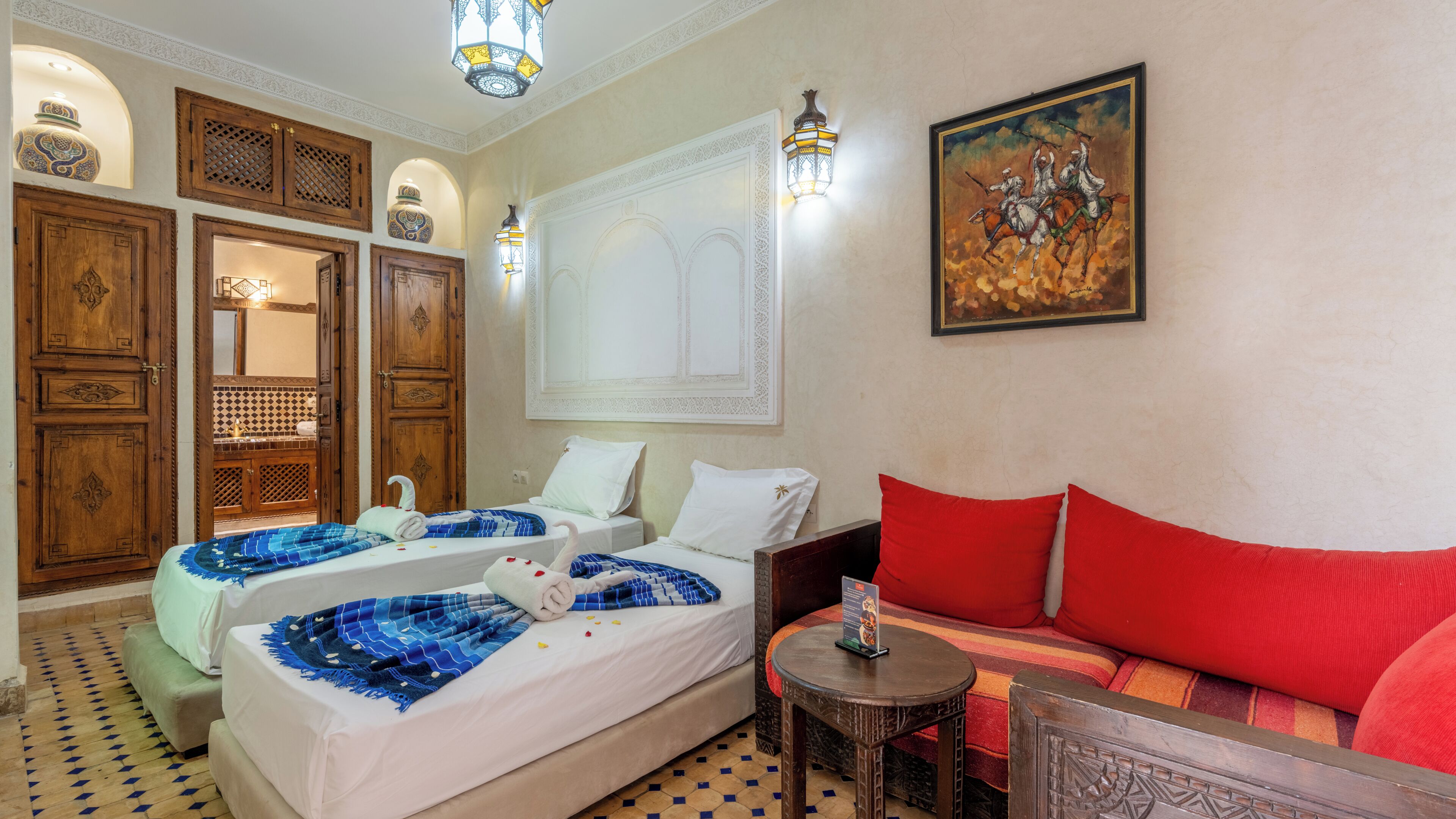A hotel room with two beds, a sofa, a small table, and a painting on the wall.