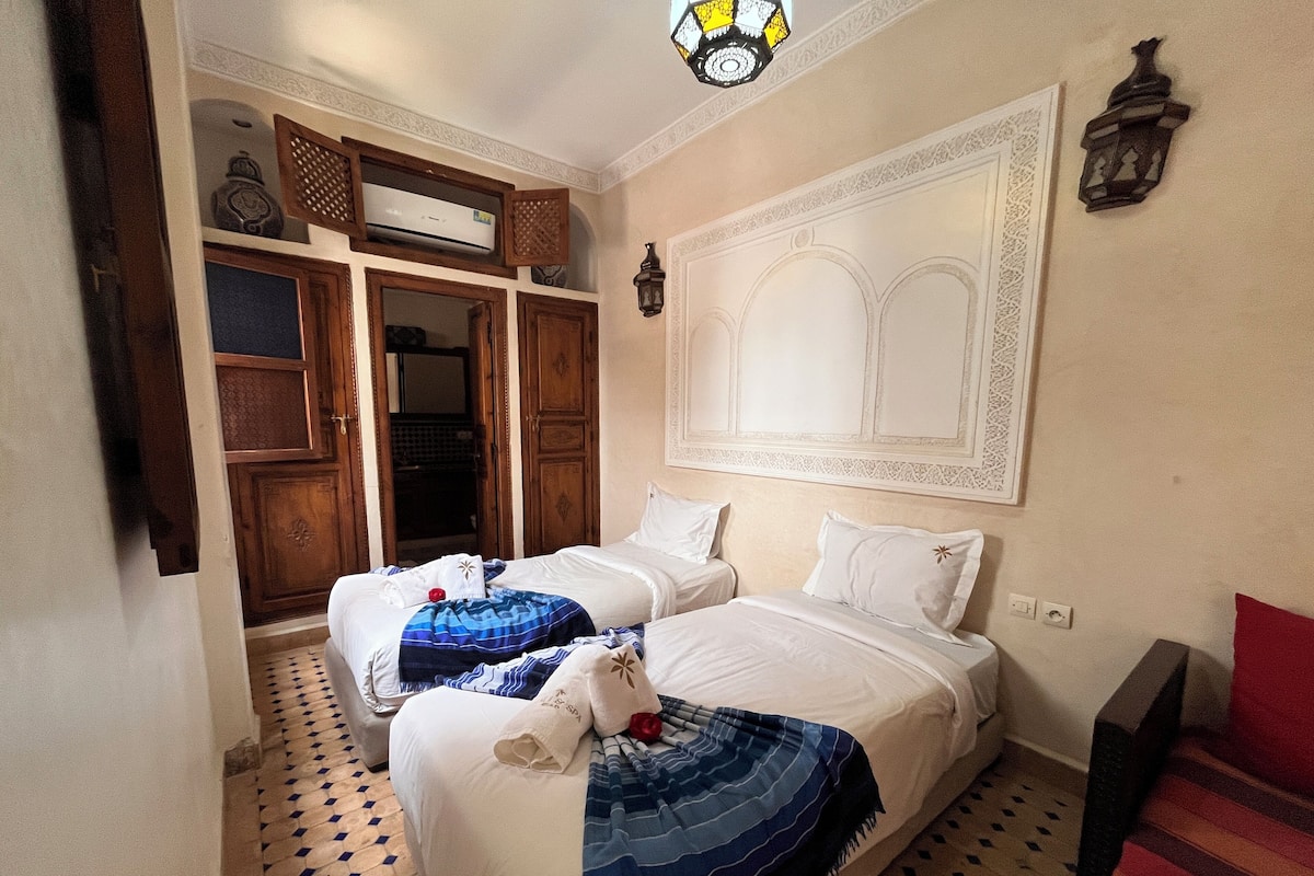 Een hotelkamer met twee bedden, een groot decoratief wandkunstwerk, een plafondlamp en een vloer met patroon.