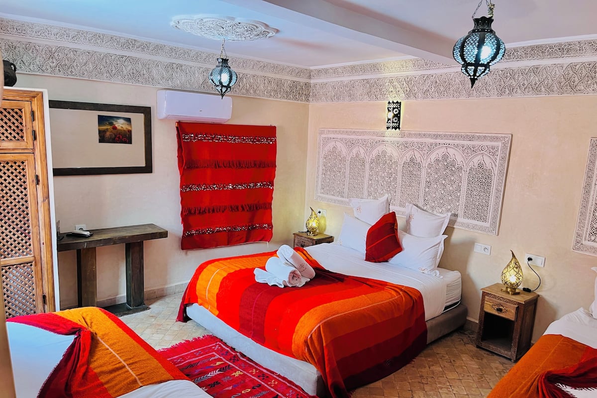 Een hotelkamer met een groot bed, twee nachtkastjes, een rood gordijn en decoratieve wanddecoraties.
