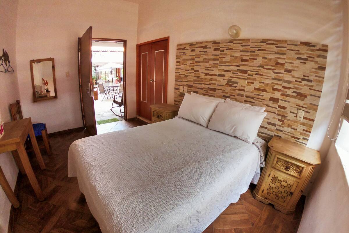 Un dormitorio con una cama grande, cabecera de madera, mesitas de noche y una pequeña mesa con sillas.
