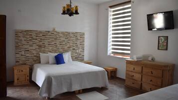 A bedroom with a bed, wooden nightstands, a dresser, a TV, and a window with blinds.