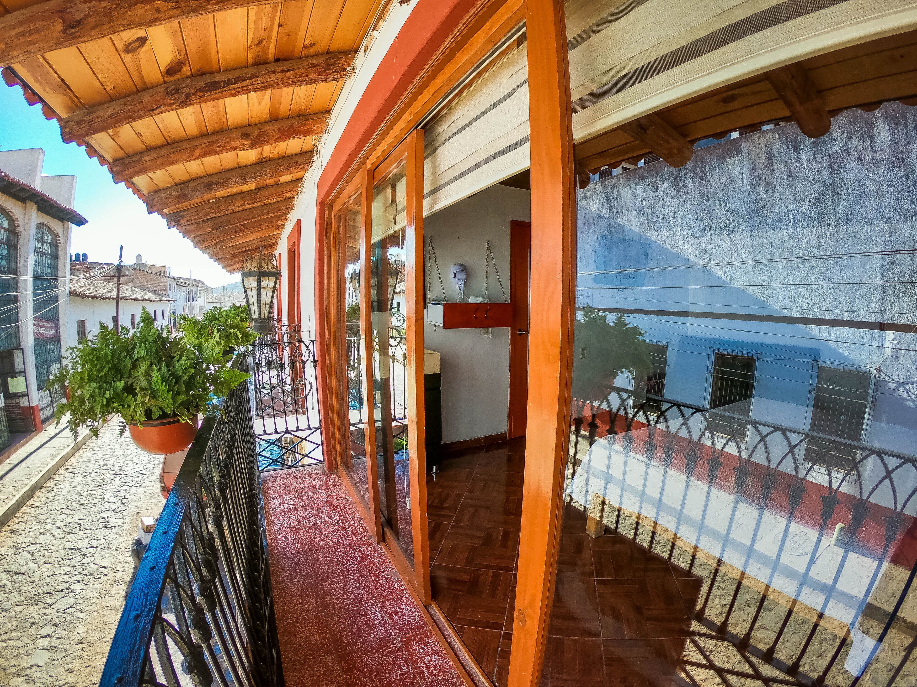 Un balcon en bois doté d’un sol carrelé de tuiles rouges, d’une plante en pot et d’une rambarde en métal.