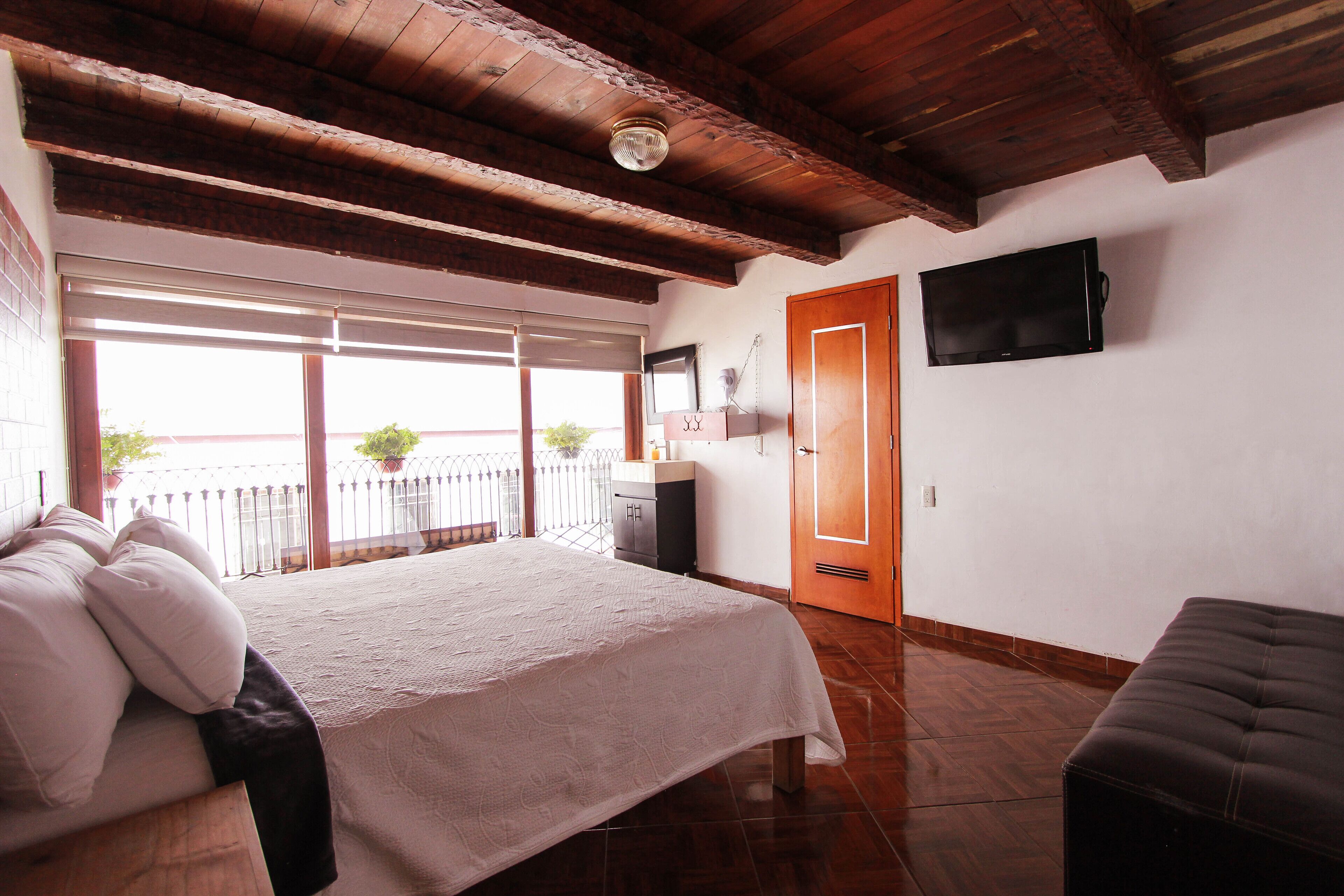 A bedroom with a bed, a television, a wooden bench, and a balcony with plants.