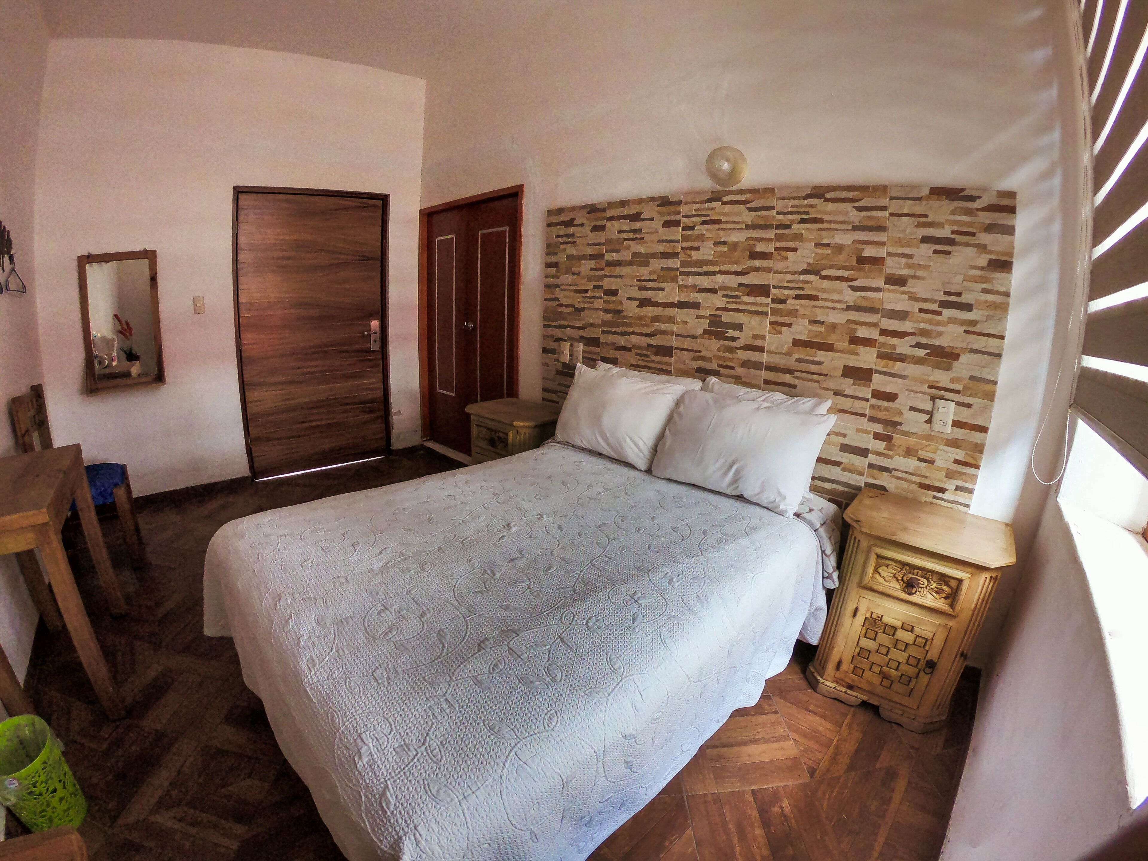 Une chambre à coucher avec un lit, une tête de lit en bois, une table de chevet, une petite table et un miroir.