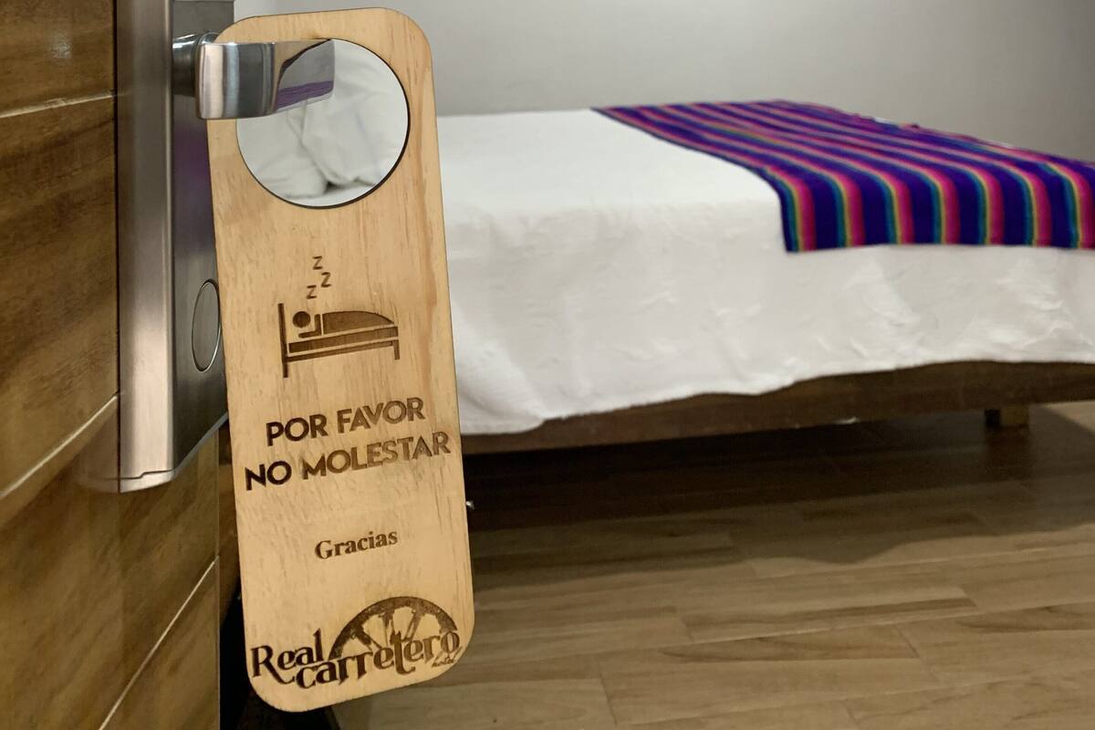 Una habitación de hotel con puerta de madera, una cama con manta a rayas de colores y un dispensador de toallas en la pared.