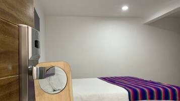 A hotel room with a wooden door, a bed with a colorful striped blanket, and a wall-mounted towel dispenser.