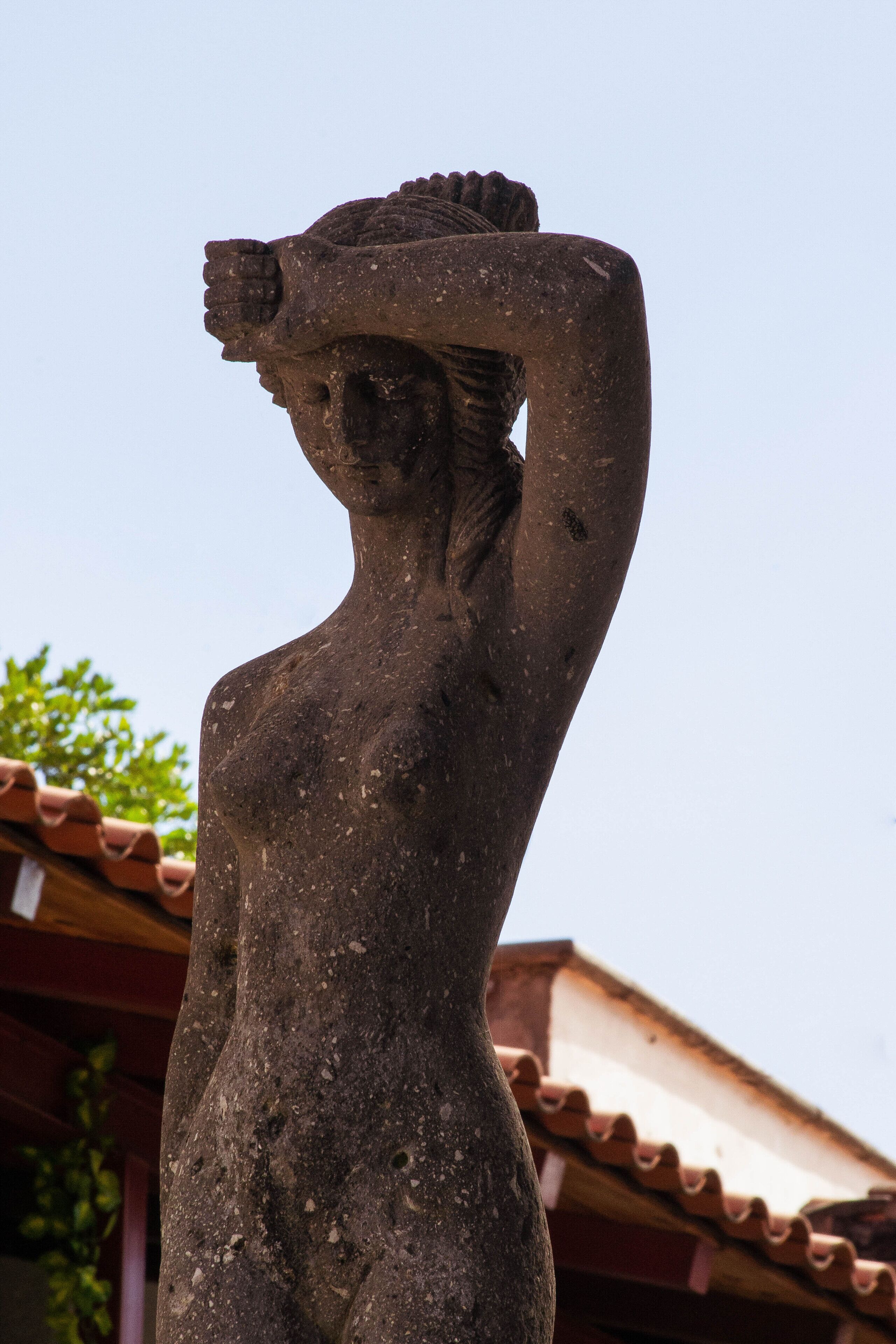 A stone statue of a woman with one arm raised, standing outdoors.