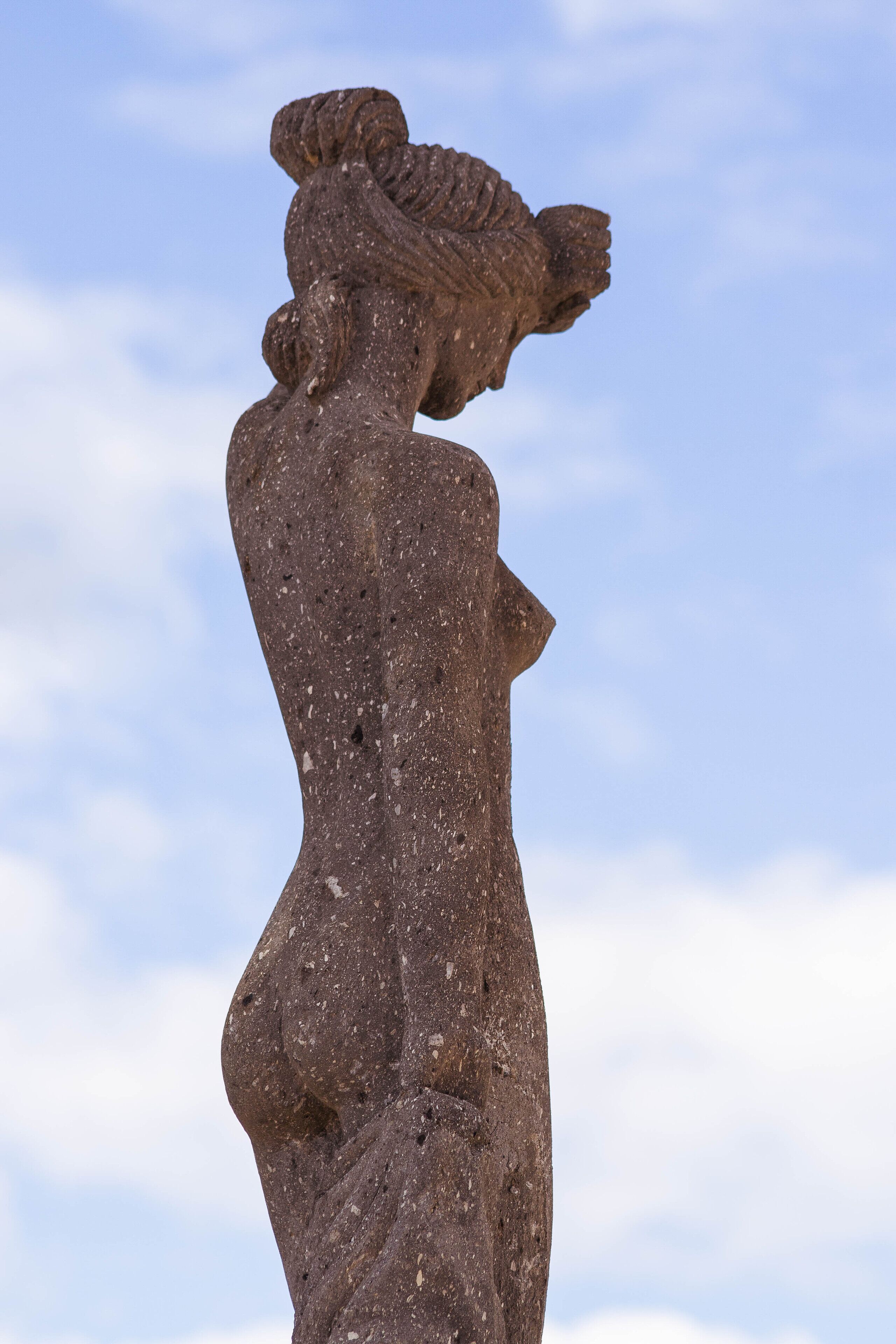 A stone sculpture of a woman with a detailed headdress, set against a clear sky.