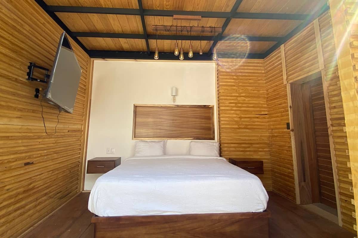 Un dormitorio con paneles de madera, una cama, mesitas de noche y un televisor montado.