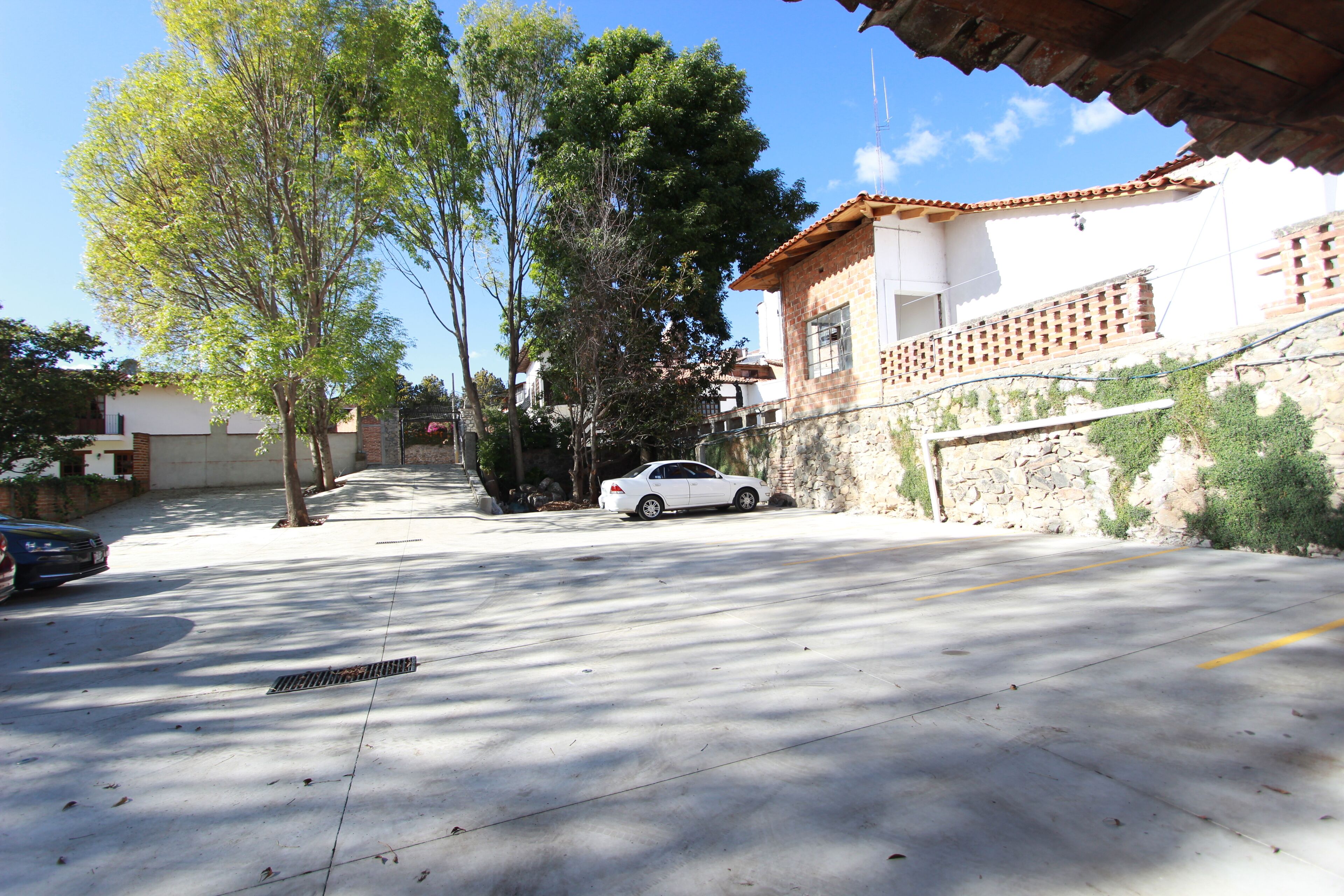 Uma rua com um carro branco estacionado na lateral, árvores ao longo da estrada e um prédio com telhado de azulejos.