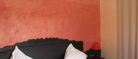 Habitación de hotel con cama, mesita de noche, lámpara y un equipo de aire acondicionado en la pared.