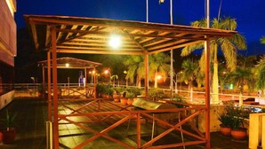 A covered outdoor seating area with a metal frame and a roof, surrounded by potted plants and palm trees. - Dynasty Hotel Miri (Miri)