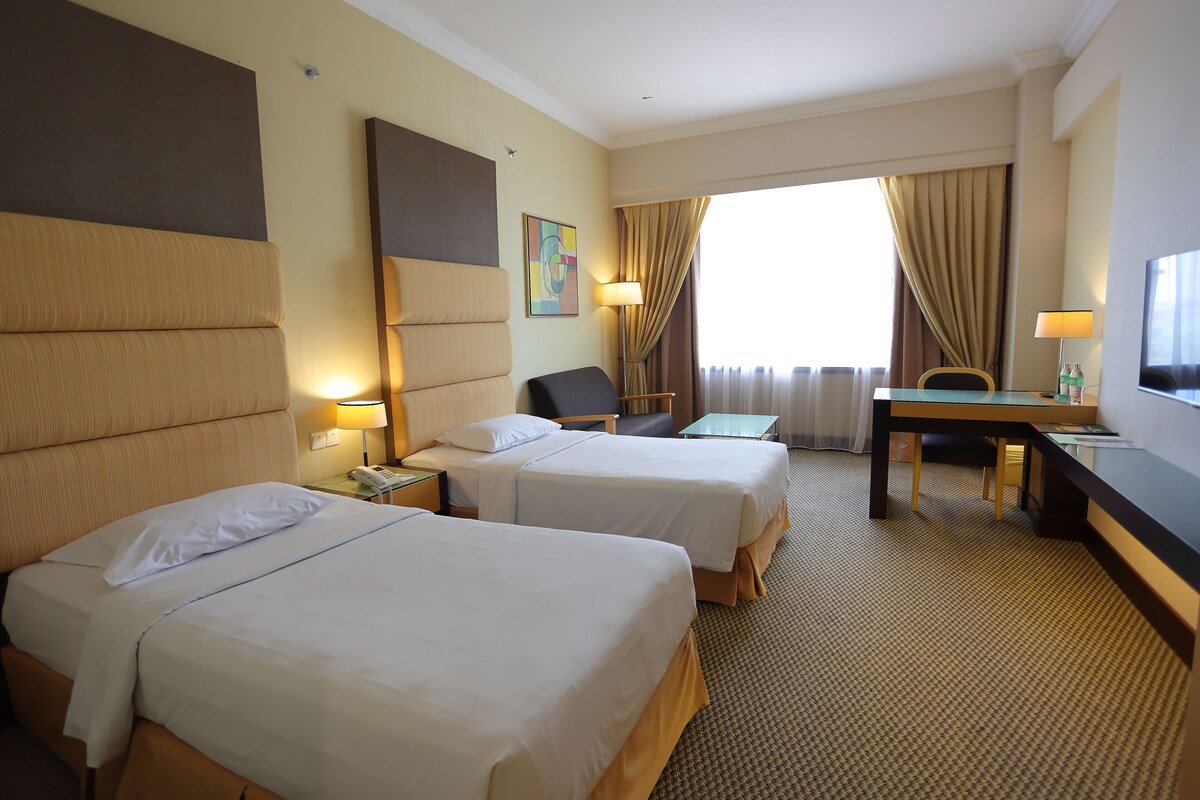 Habitación de hotel con dos camas, un escritorio, una silla y un televisor.
