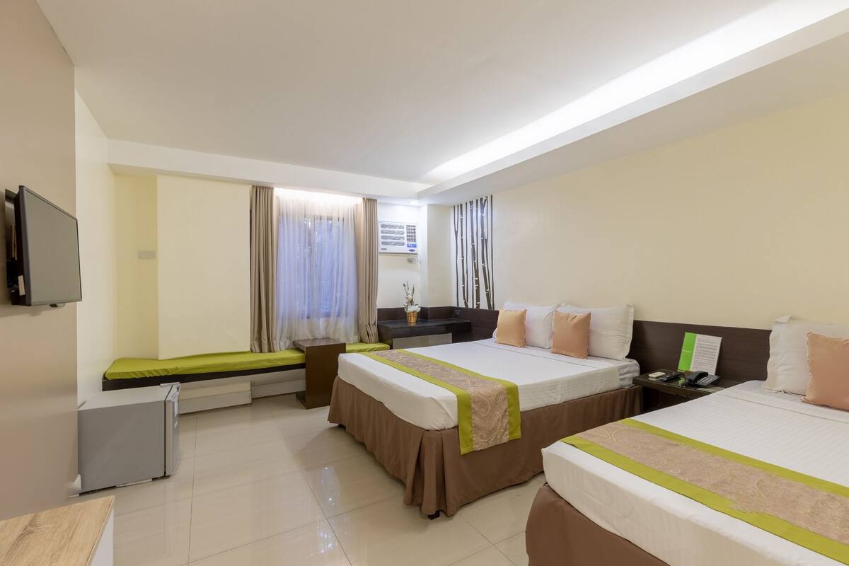 A hotel room with two beds, a desk, a small fridge, and a TV.
