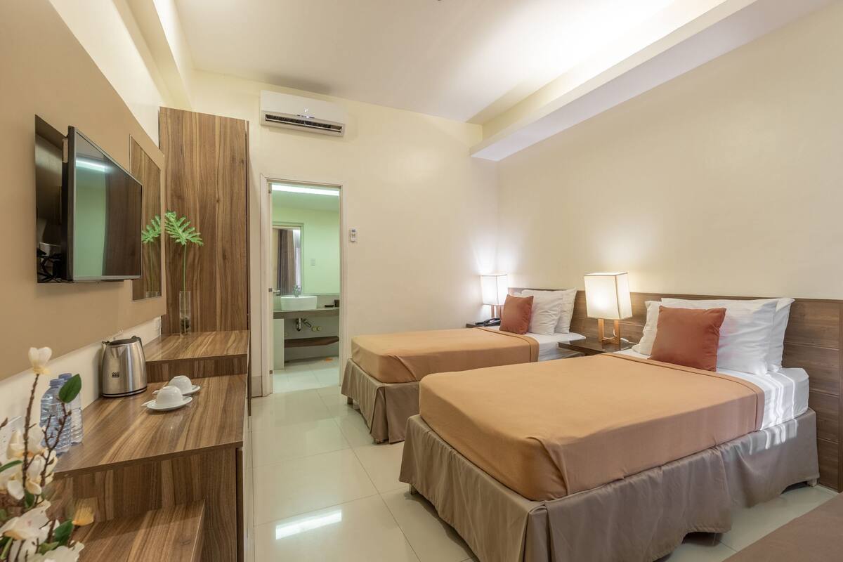 A hotel room with two beds, a desk, a TV, and a bathroom visible through an open door.