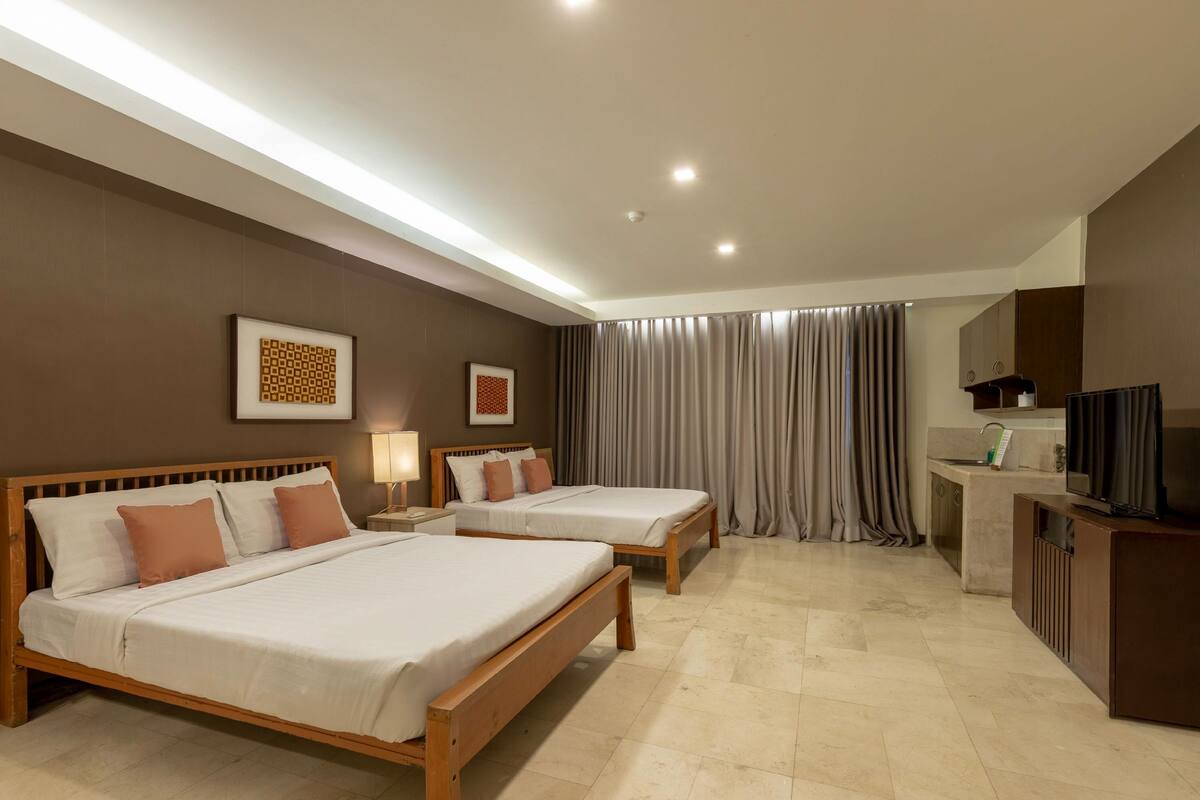 A hotel room with two wooden beds, a small kitchenette, and a TV.