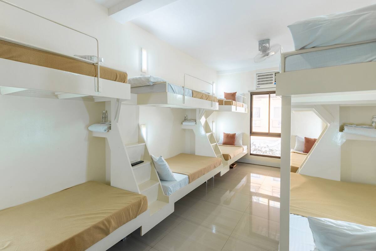 A bunk room with multiple beds, a window, and a door.