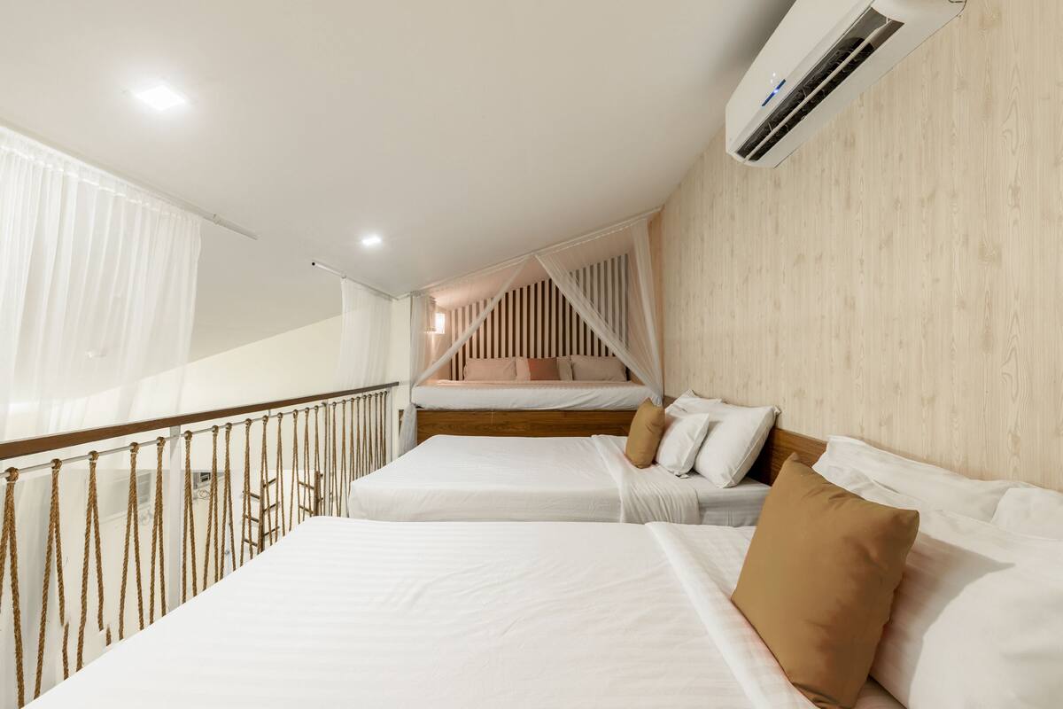 A hotel room with two beds, a balcony with a railing, and an air conditioning unit on the wall.