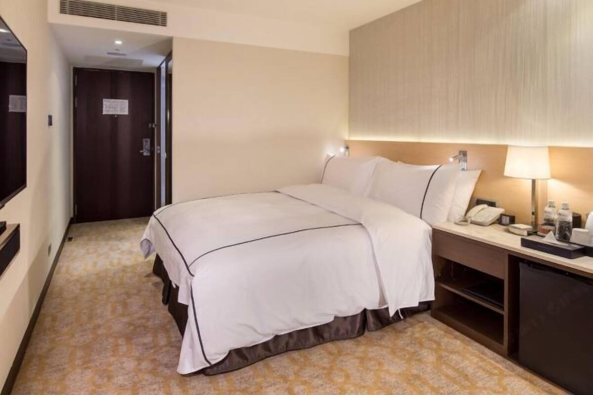 A hotel room with a bed, bedside table, lamp, and a door.
