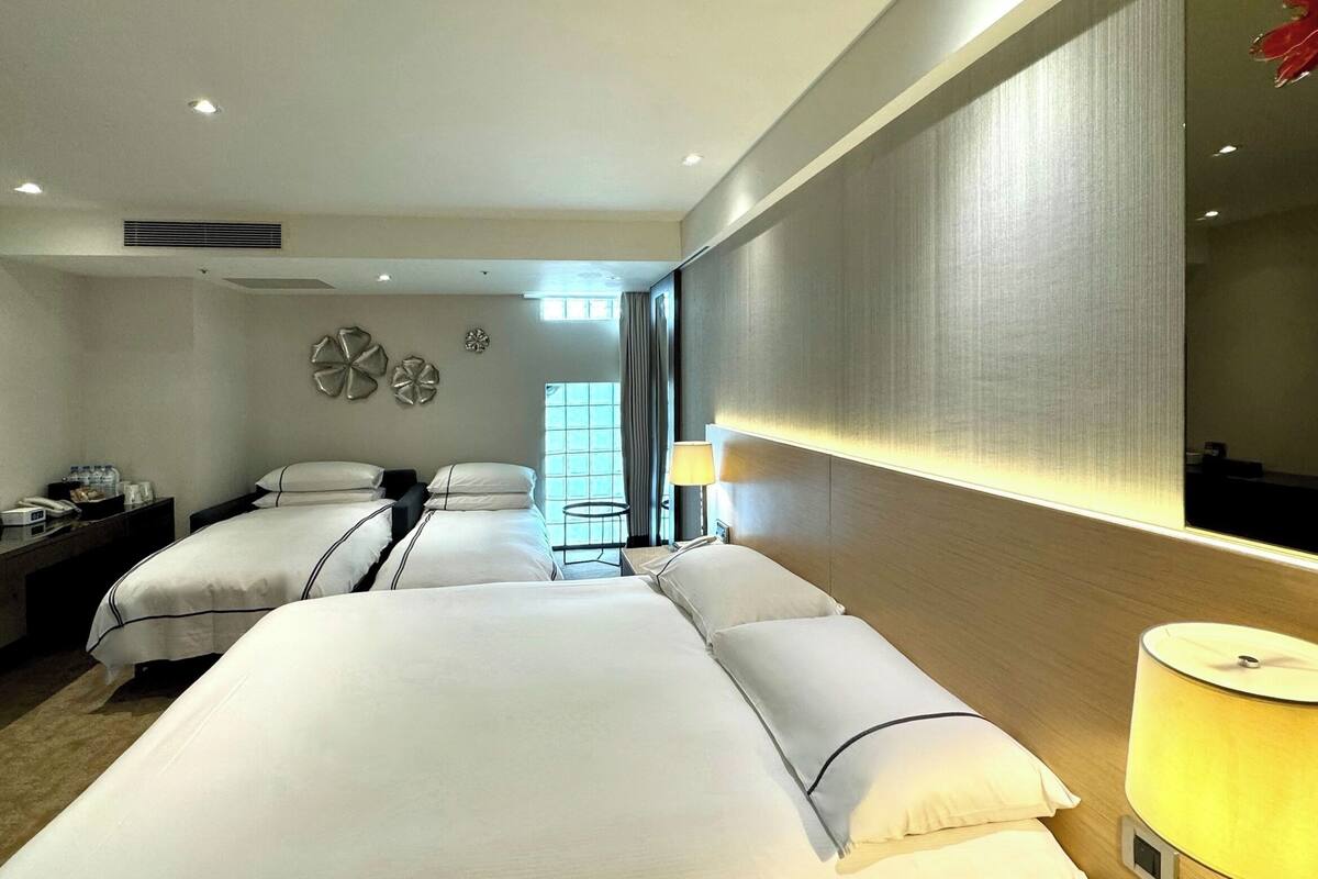A hotel room with two beds, a bedside table, a lamp, and a large mirror.