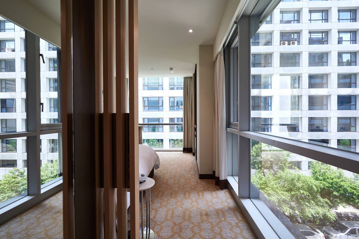 A hotel corridor with large windows, a bed, and a small table.