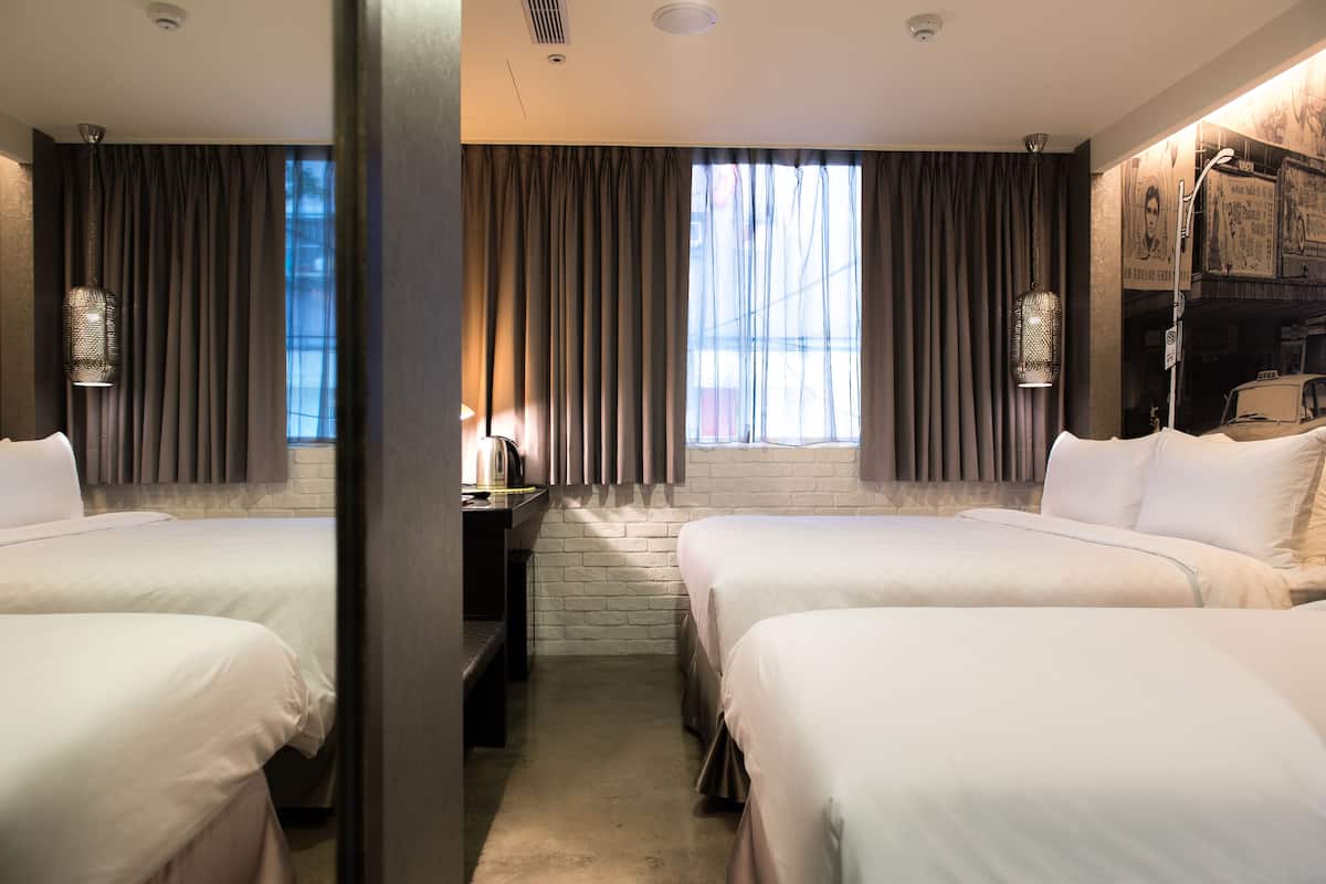 Quarto de hotel com duas camas, uma escrivaninha e uma janela grande com cortinas.