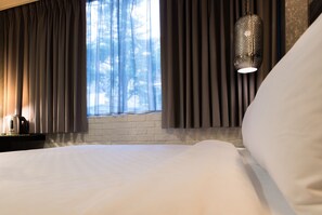 Habitación de hotel con una cama grande, ventana con cortinas, lámpara colgante y pared de ladrillo.
