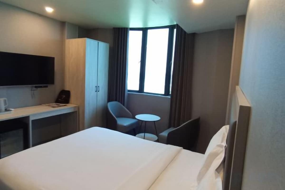 A hotel room with a bed, a desk, a chair, a small table, and a TV.